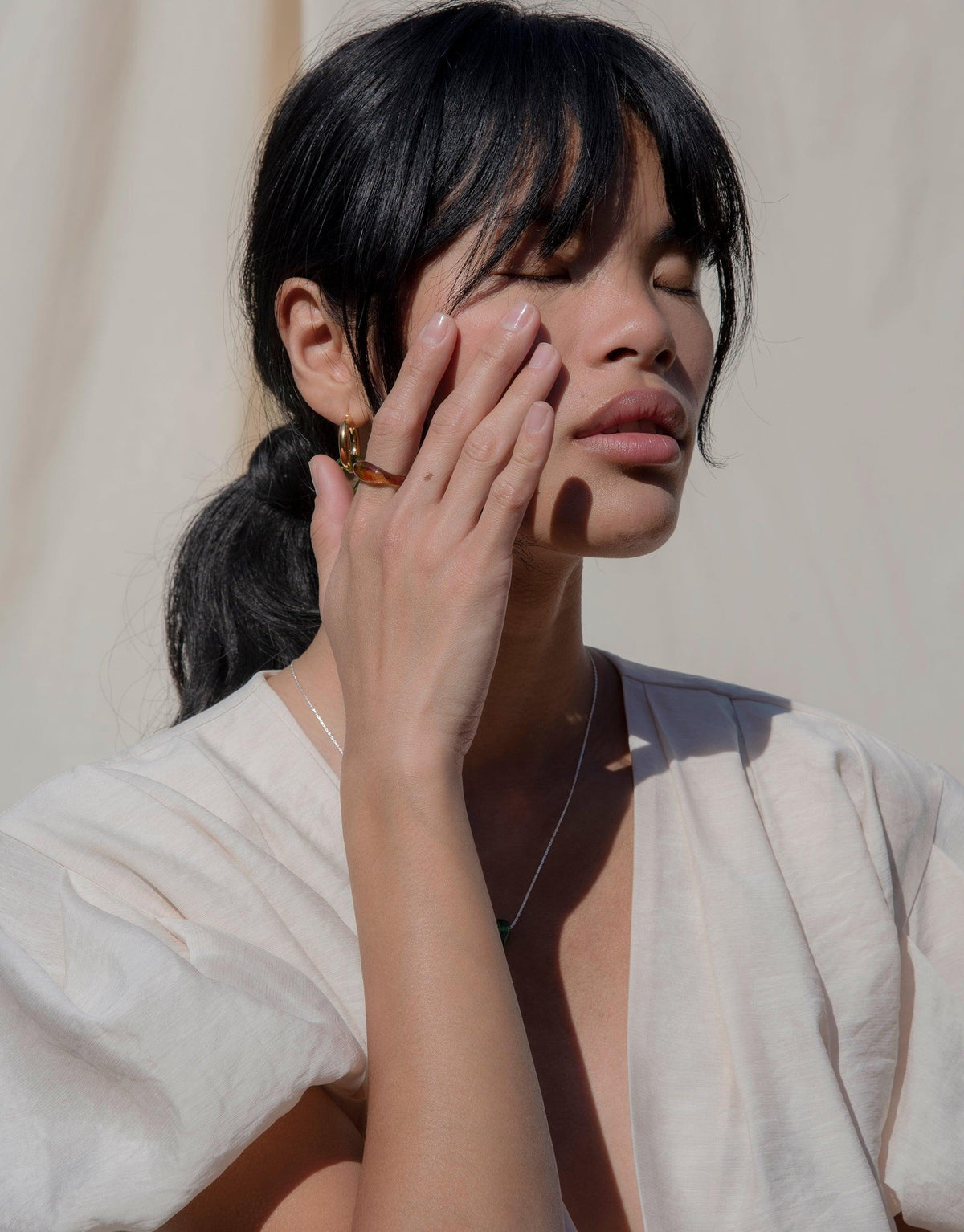 Person wearing Engravable Signet Ring from CLED's Messenger Collection, showcasing eco-friendly jewelry. Hand touching face to highlight ring, demonstrating elegant design and personalized etching. Sustainable fashion statement piece made in Los Angeles. CLED