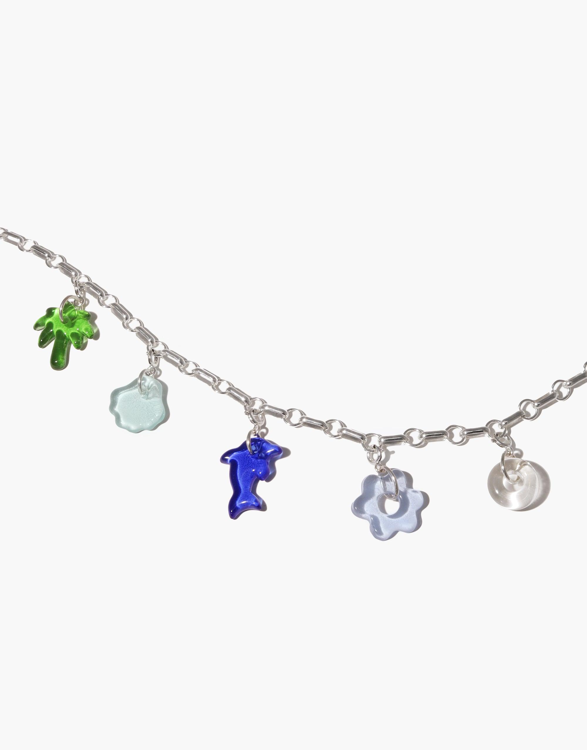 Silver chain bracelet with colorful glass charms including green palm tree, blue dolphin, and flower shapes. Avens Icon Charm by CLED, showcasing upcycled eco gems in various playful designs.