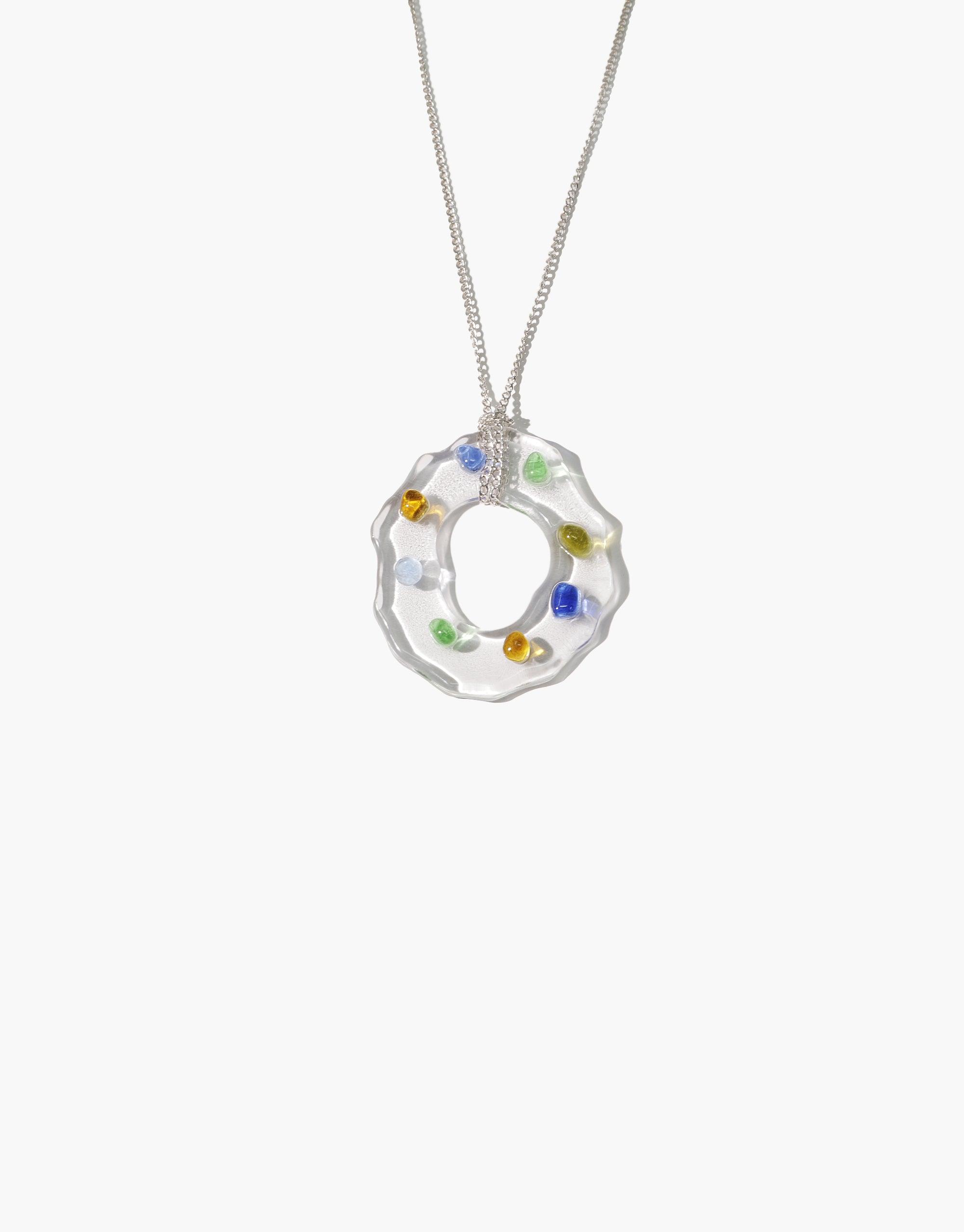 High Tide Necklace in Spectrum featuring a unique circular pendant with colorful eco gems embedded in clear glass, suspended on a delicate silver chain. Handcrafted from upcycled glass bottles, this sustainable jewelry piece reflects prismatic hues reminiscent of natural light refraction. CLED