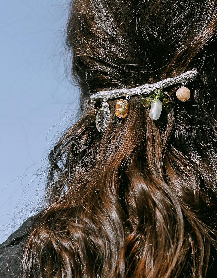 Floral Barrette adorned with colorful eco-friendly glass charms on a sterling silver base, elegantly fastened in dark wavy hair against a blue sky background. Handcrafted hair accessory featuring repurposed materials. CLED