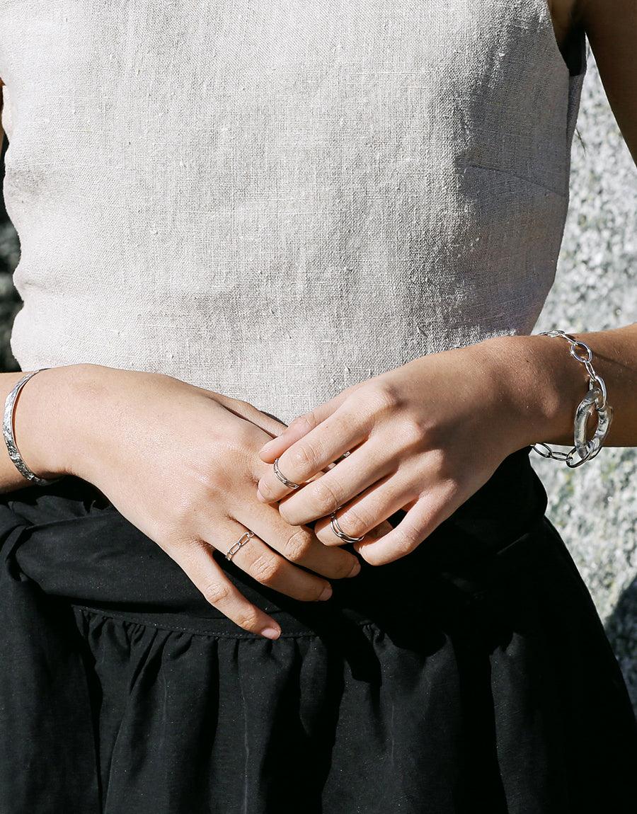 Elegant hands wearing multiple rings and a sterling silver oval chain bracelet, showcasing the High Tide Oval Chain Bracelet's stylish design. The bracelet features a unique, organic shape complementing the wearer's wrist. Handcrafted sustainable jewelry by CLED.