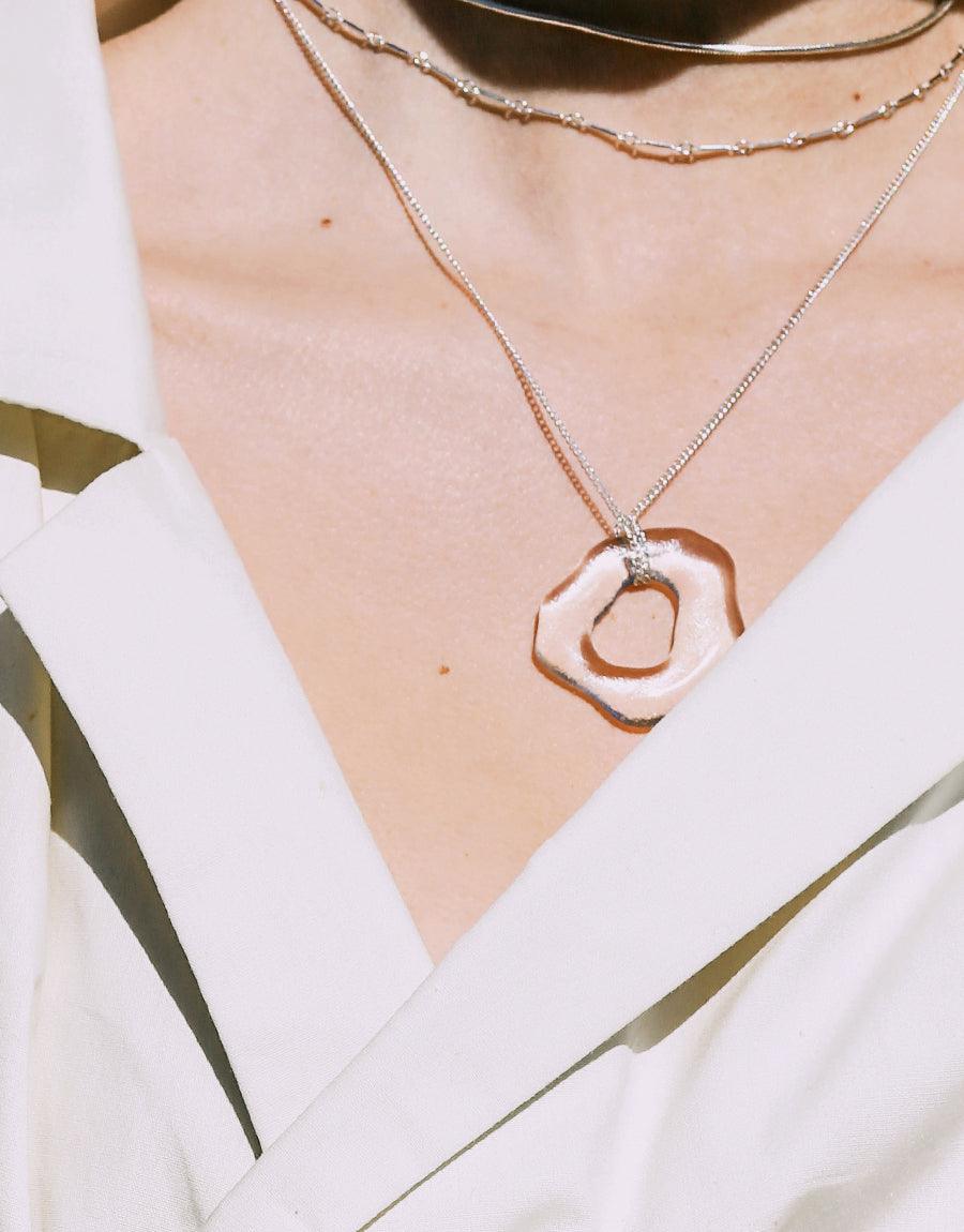 Sterling silver High Tide Necklace with organic-shaped pendant made from eco-friendly repurposed glass, layered with delicate chain necklaces. Sustainable ocean-inspired jewelry perfect for everyday wear. Handcrafted in Los Angeles by CLED.