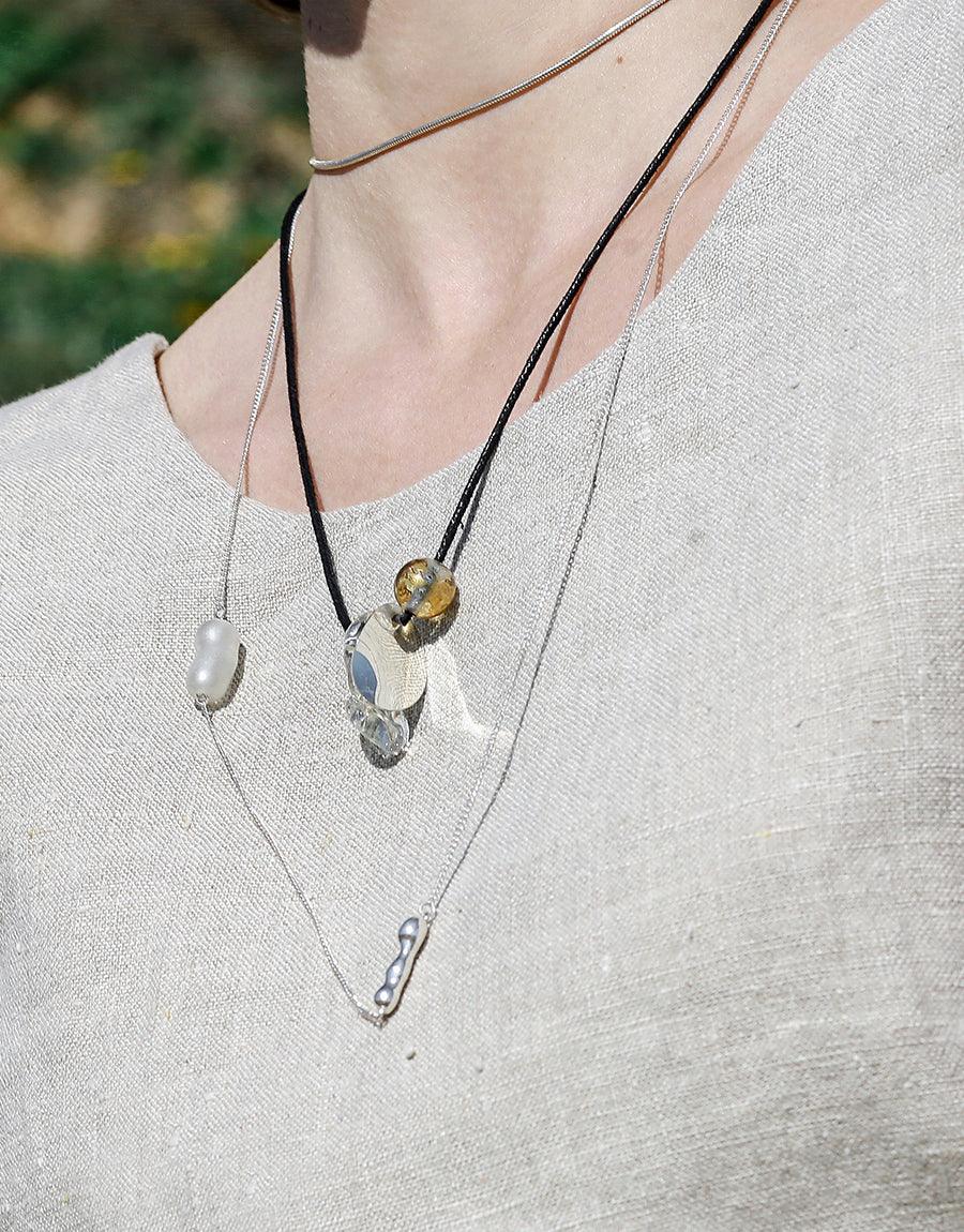 Layered necklaces featuring sustainable Eco Gem pearls and water drop pendants on delicate chains, showcasing the Shoreline Long Necklace's versatile style. Handcrafted sterling silver jewelry with repurposed glass elements, perfect for eco-conscious fashion. CLED Shoreline Long Necklace.