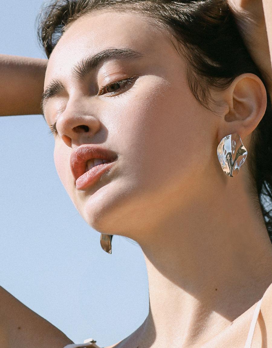 Wave Earrings in organic, wavy design, showcased on a woman with her hand behind her head. The sterling silver, nature-inspired earrings offer an artful, eco-conscious look, made in Los Angeles.