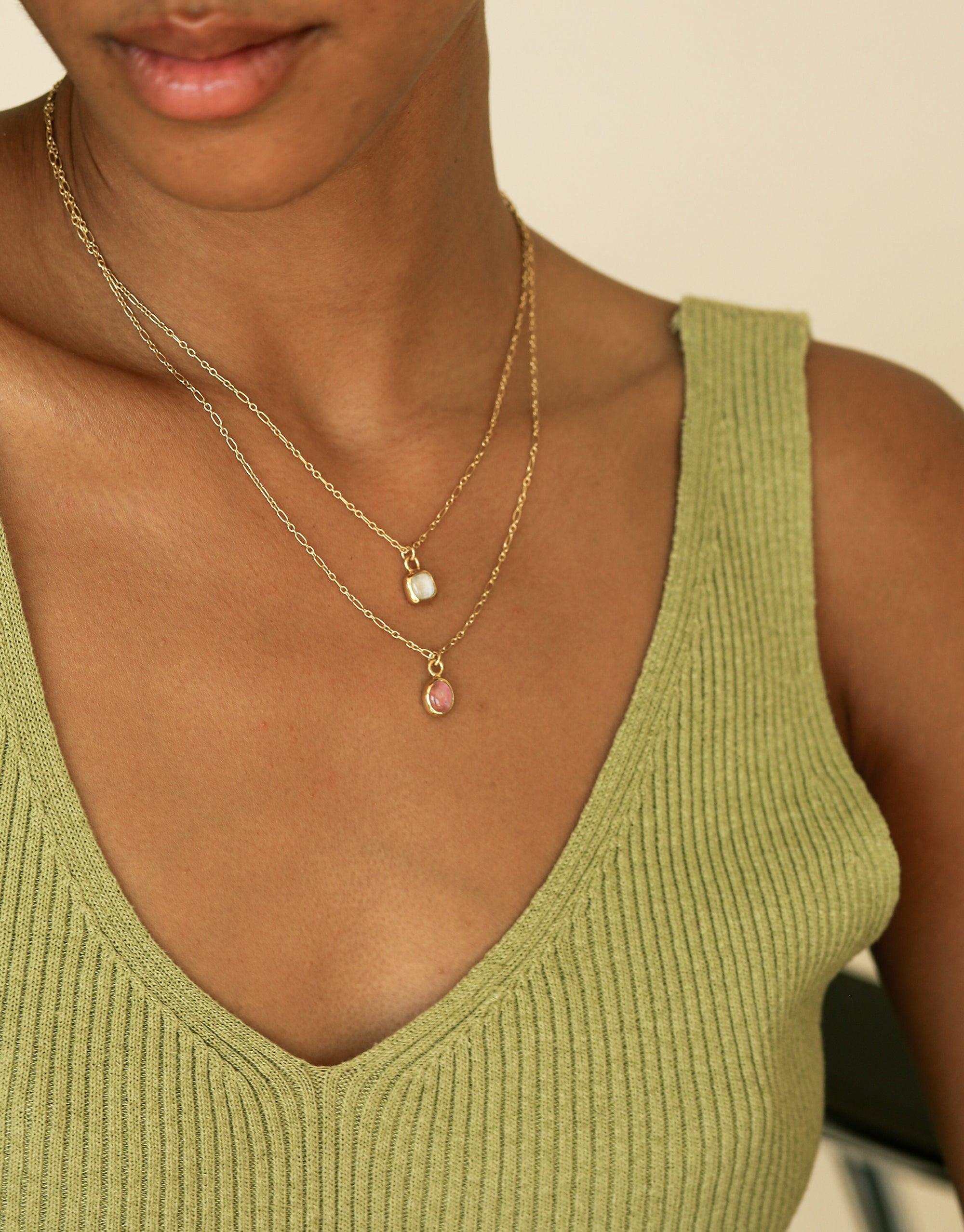 Close-up of a person wearing a green ribbed top and delicate gold layered necklaces with small oval charms. The necklaces feature dainty chains and subtle pendant details, showcasing the Oval Charm Necklace by CLED.