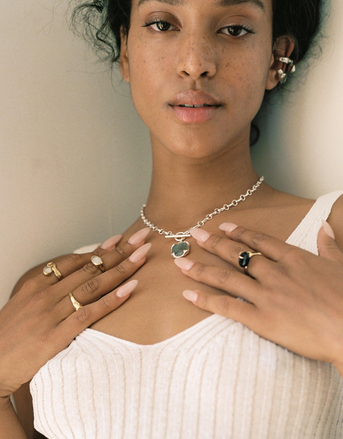 Close-up of model wearing delicate silver chain necklace with eco-friendly glass pendant, multiple rings including Oval Dangling Ring, and white ribbed top. Showcases handcrafted jewelry made from upcycled materials. CLED, Oval Dangling Ring.