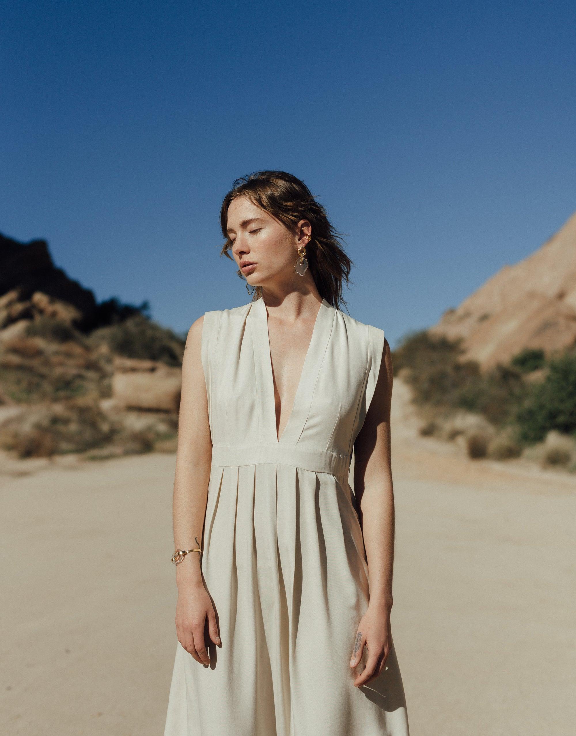 Woman in white dress standing in desert landscape, wearing Canyon Earrings inspired by terrain formations. Handcrafted eco-friendly jewelry showcasing organic shapes and recycled glass. Sustainable fashion accessory by CLED.