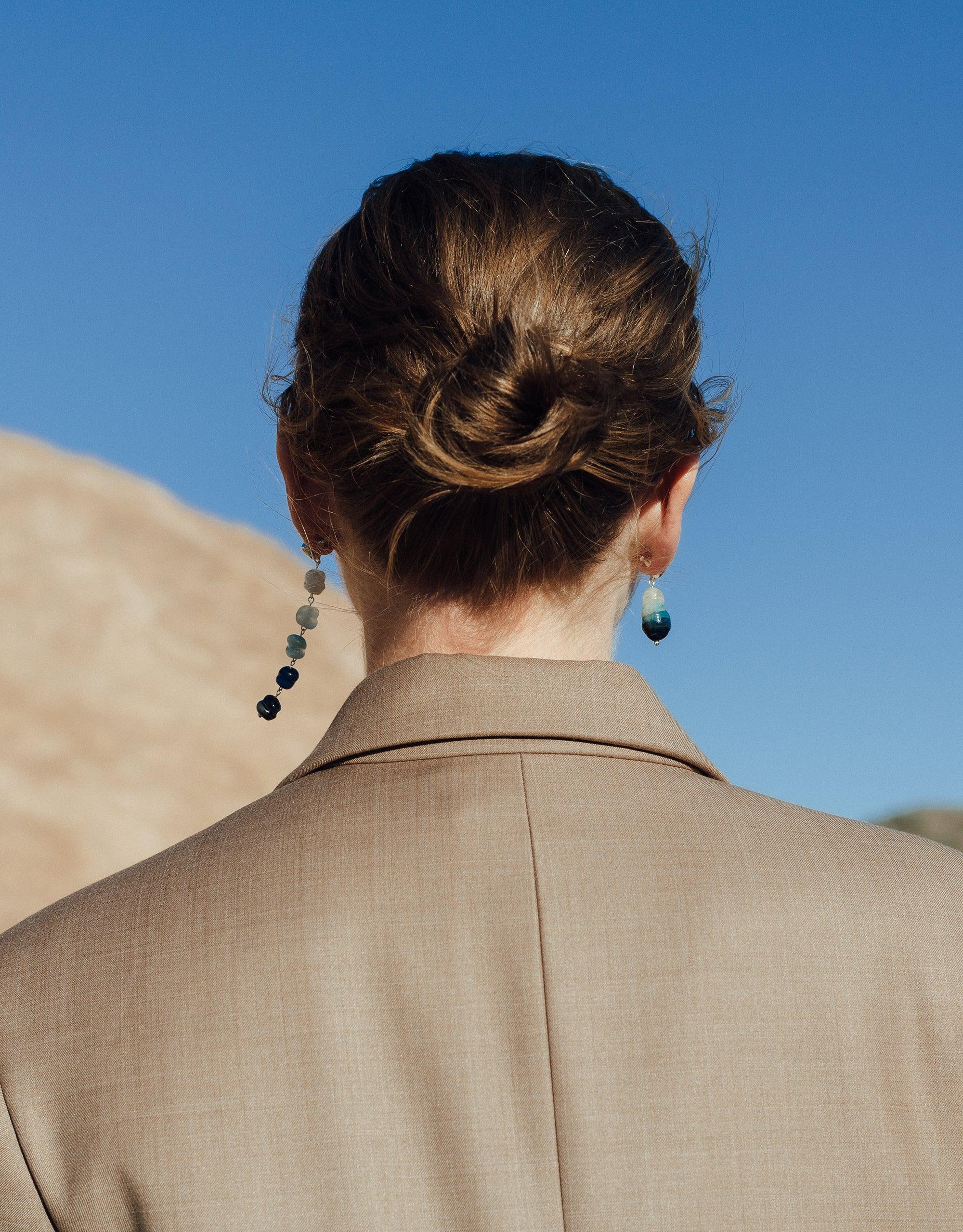 Back view of person wearing Shades of Nature | Waterfall Earrings, showcasing cascading blue glass beads against desert backdrop. Eco-friendly jewelry inspired by canyon terrain, handcrafted in Los Angeles. Sustainable fashion accessory by CLED.