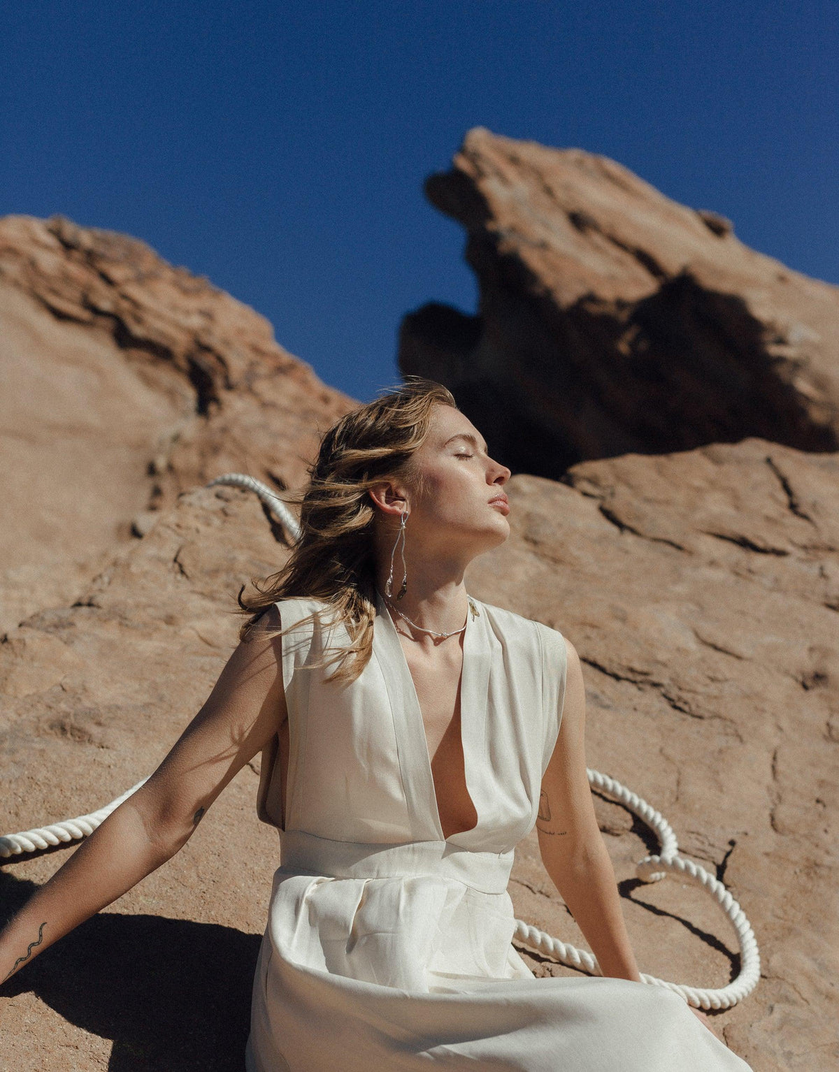Woman in white dress against canyon backdrop, wearing Rope Drop Earrings. Earrings feature abstract shapes inspired by rock climbing ropes and eco-friendly glass drops, embodying the Terrain Collection's canyon-inspired design. Handcrafted jewelry by CLED.