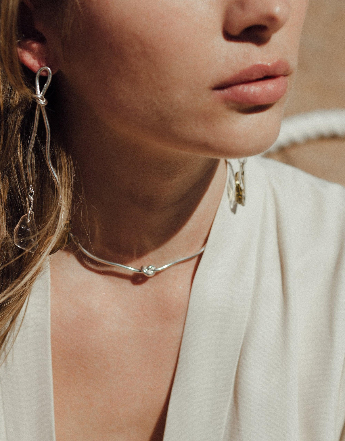 Close-up of a person wearing a sleek silver Rope Hook Necklace, showcasing its elegant design against a white top. The necklace's minimalist style complements the wearer's natural beauty, embodying the Terrain Collection's canyon-inspired aesthetic. CLED Rope Hook Necklace.