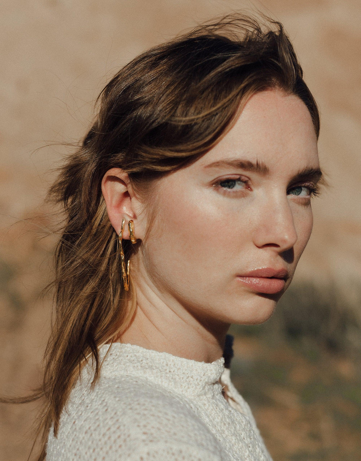 Close-up of a model wearing gold Rock Stud Earrings from the Terrain Collection, showcasing curved textured design inspired by canyon formations. Handmade in Los Angeles, available in Sterling Silver or Gold Vermeil. Rock Stud Earrings by CLED.