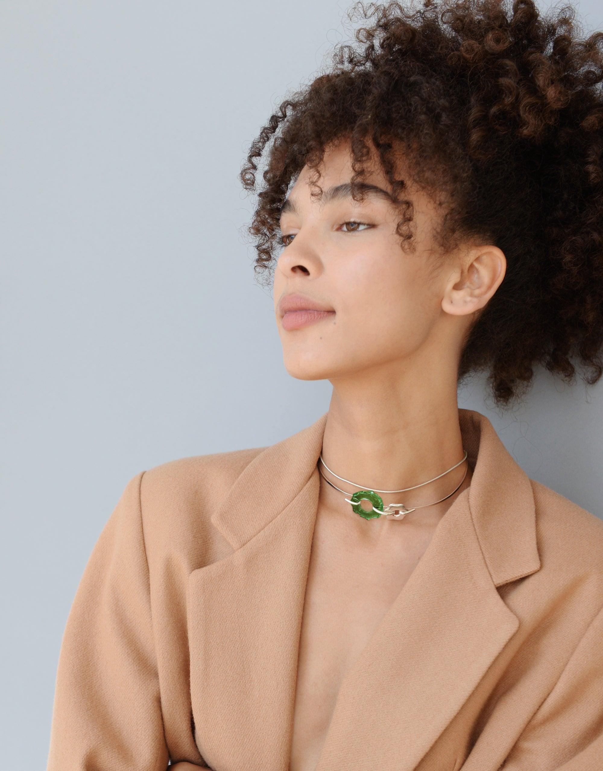 Elegant model wearing Avens Choker Necklace, featuring delicate glass drop pendant on thin metal chain. Stylish accessory paired with beige blazer, showcasing eco-friendly jewelry design inspired by Arctic flowers. Avens Choker Necklace by CLED.