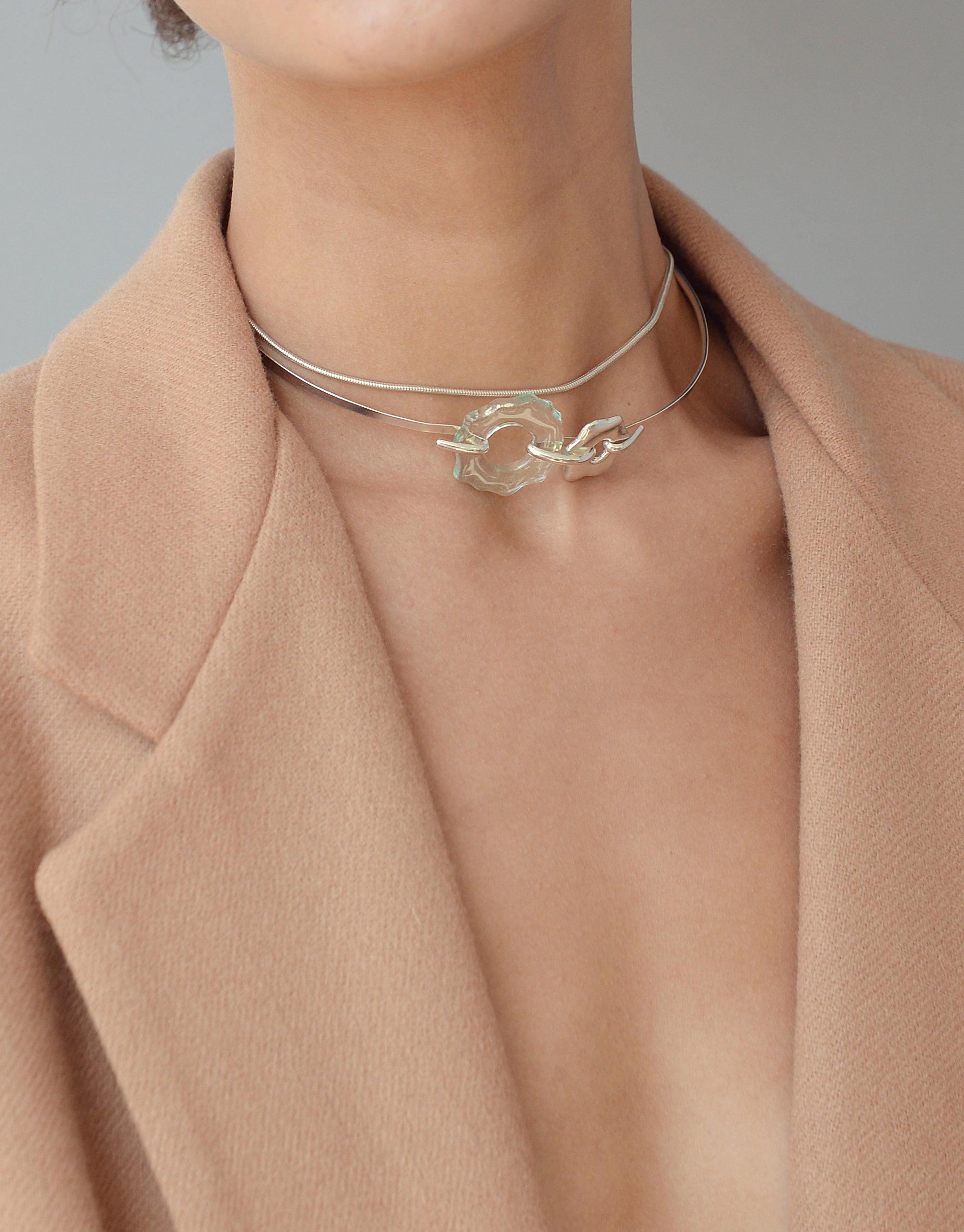 Elegant Avens Choker Necklace featuring a delicate silver chain with a transparent glass pendant, worn by a model in a beige coat. Minimalist design inspired by Arctic flora, perfect for day-to-evening wear. Eco-friendly jewelry by CLED.