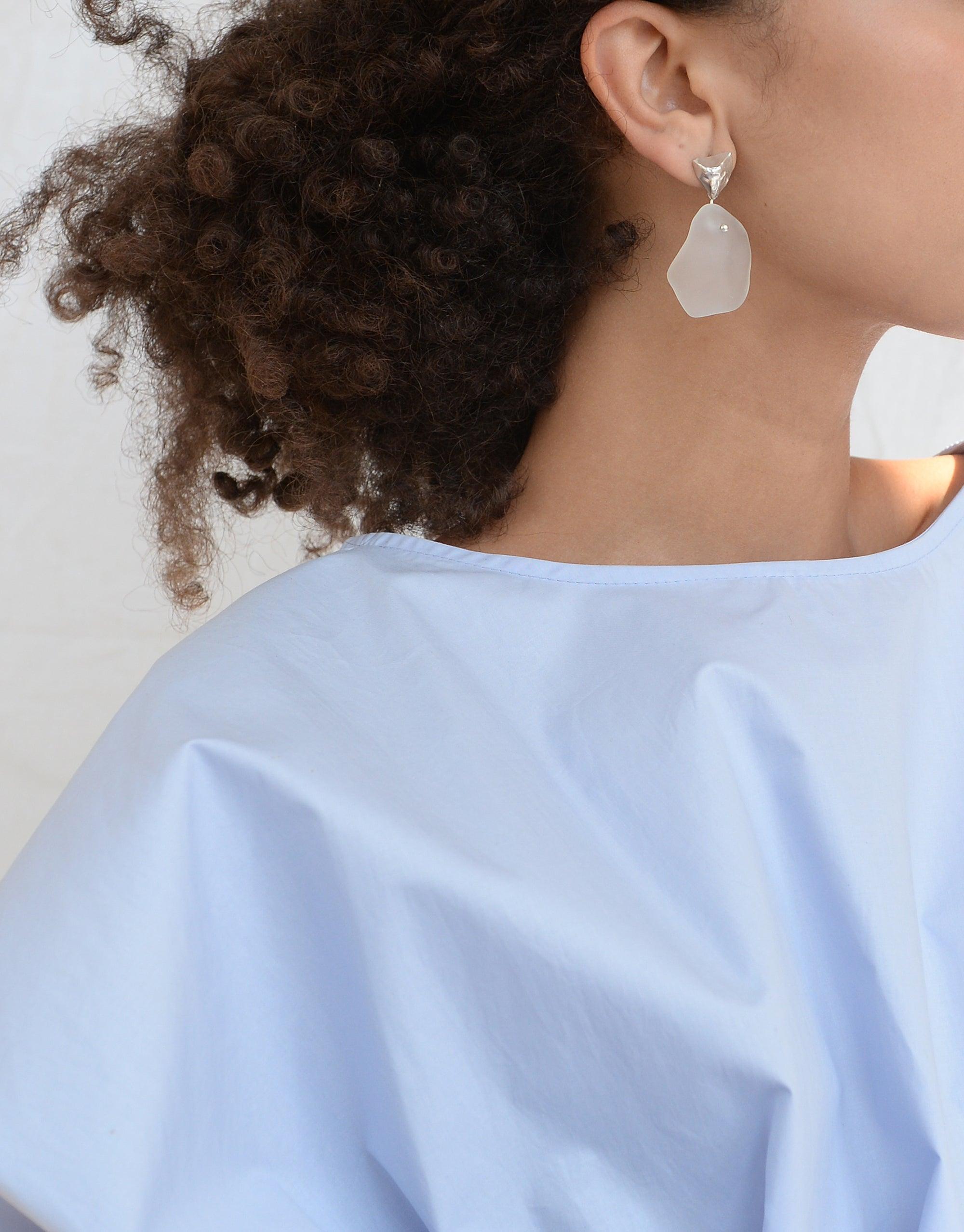 Tip of the Iceberg Earrings: A woman models eco-conscious, matte-finish earrings inspired by Arctic icebergs, featuring hand-formed Eco Gems from repurposed glass, highlighting CLED's sustainable jewelry collection.
