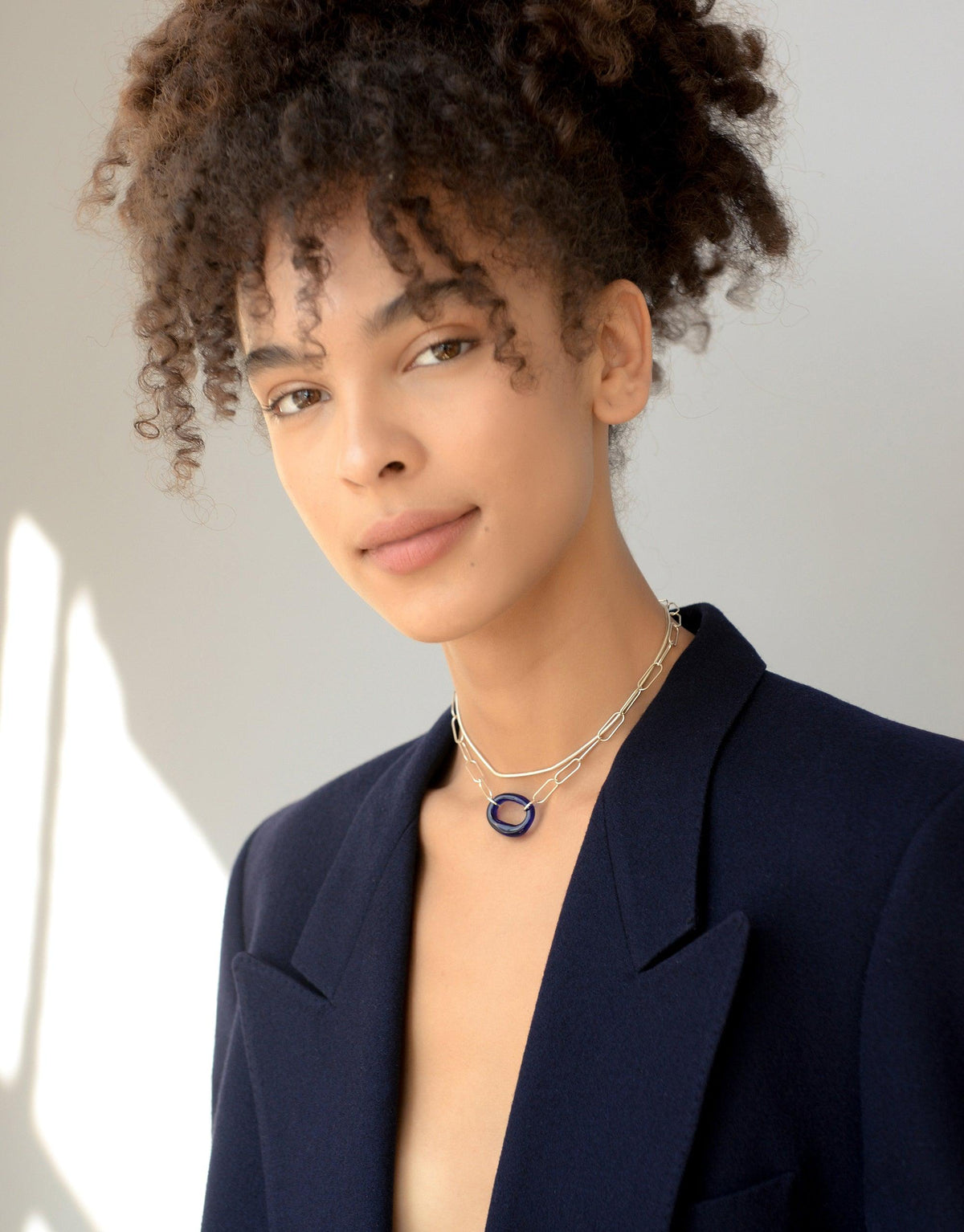The Day Loop Necklace elegantly adorns a woman's neck, showcasing an oval chain design. This minimal piece is crafted with repurposed Eco Gems, embodying CLED's eco-conscious ethos.