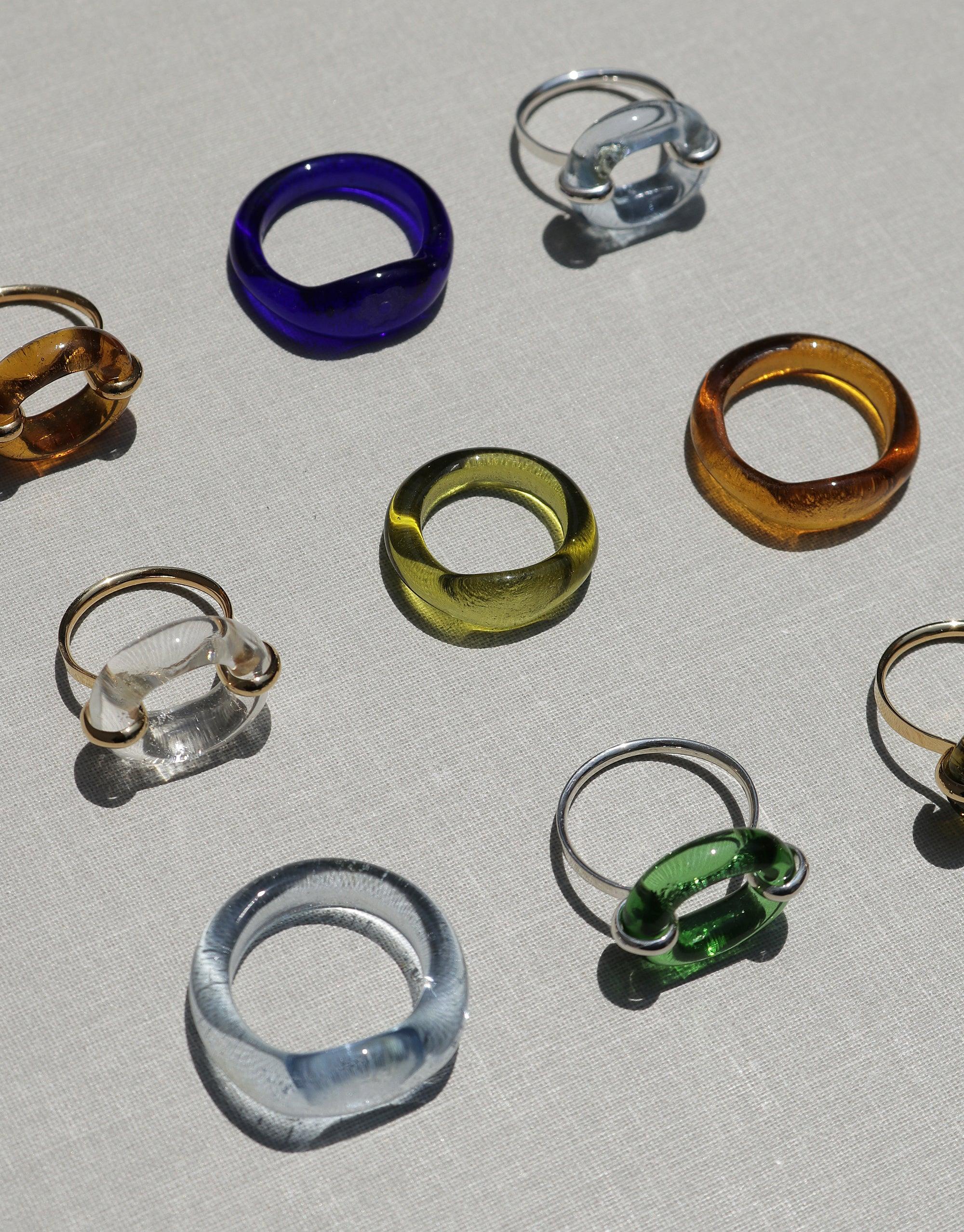 Colorful array of sustainable glass rings, including the In The Loop Ring, showcasing unique designs and shapes. Eco-friendly jewelry pieces symbolizing connection and solidarity. CLED