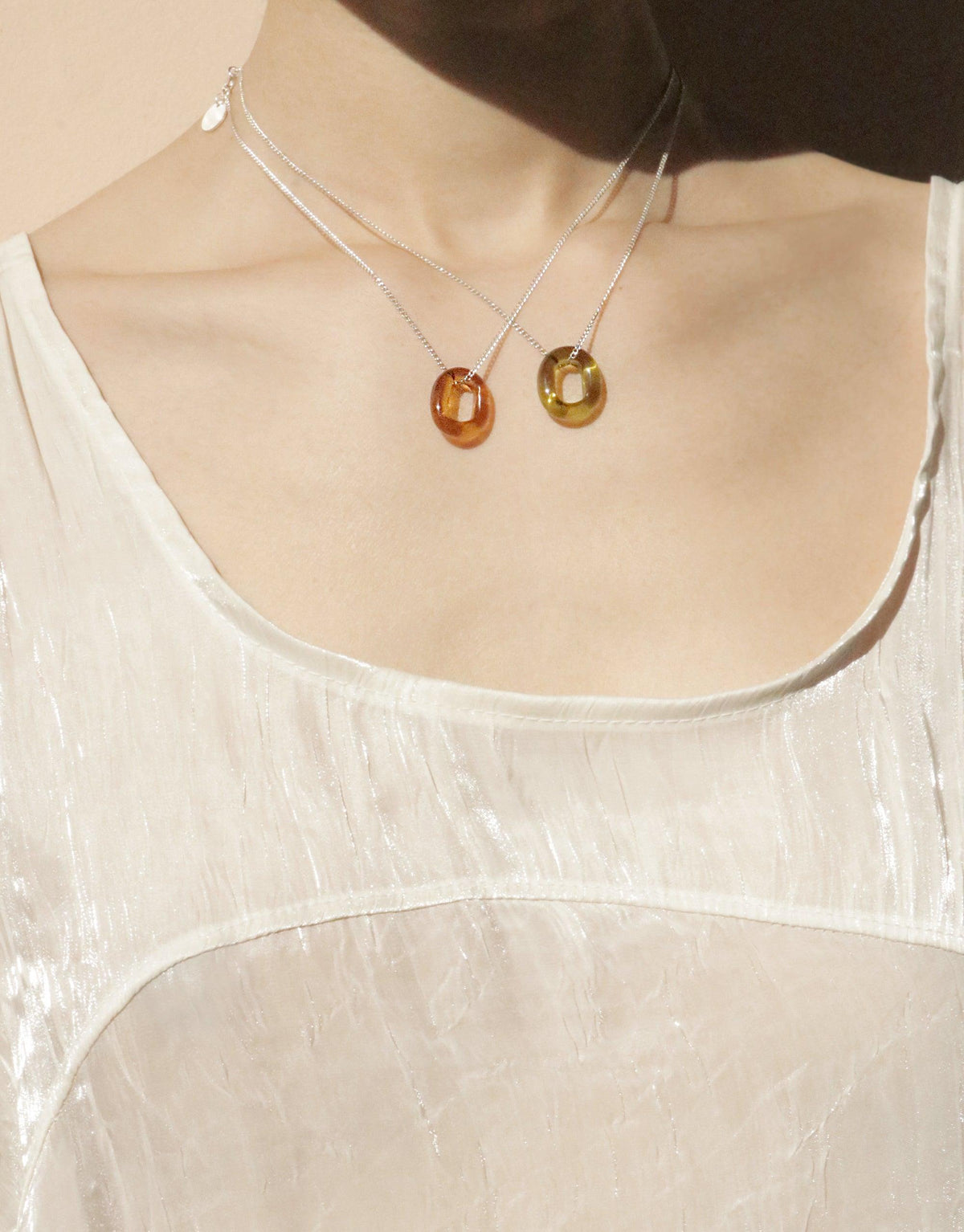 Elegant In The Loop Necklace featuring handmade eco glass pendants in amber and green hues, suspended on delicate silver chains. Minimalist design showcasing sustainable jewelry craftsmanship. Perfect for layering or wearing solo. CLED