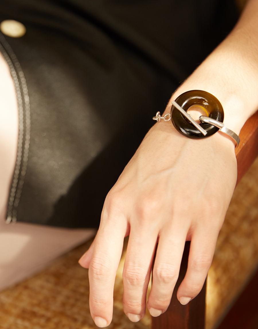 Elegant Opening Torus Toggle Bracelet featuring a handcrafted glass circle on a silver cuff, showcasing sustainable luxury and timeless design. Worn on a wrist against a dark background, highlighting its unique craftsmanship. CLED