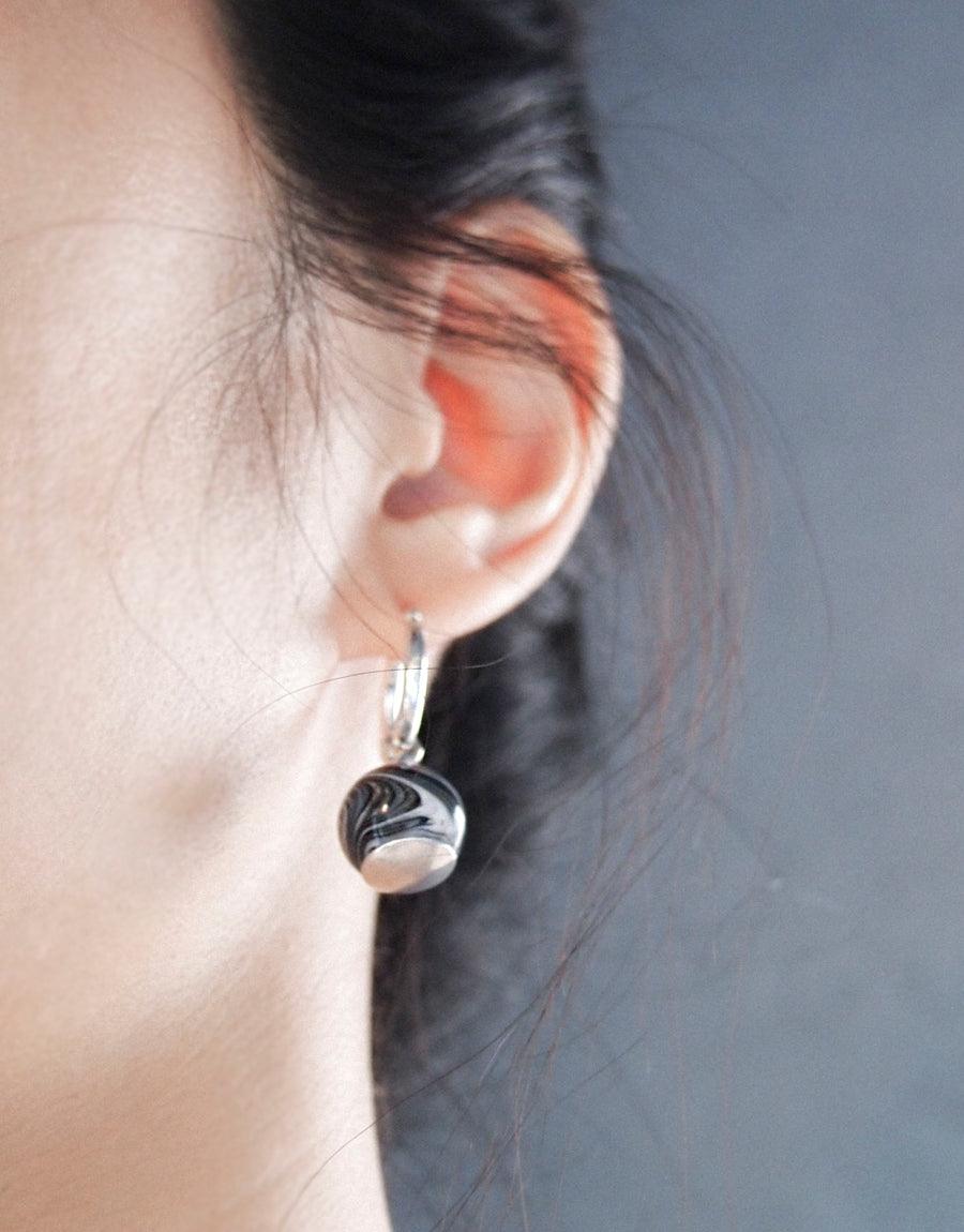 Close-up of an ear wearing elegant Drop Hoop Earrings featuring a marble glass pendant on sterling silver hoops. The earring showcases a unique swirled pattern, highlighting the handcrafted nature of CLED jewelry. Drop Hoop Earrings by CLED.