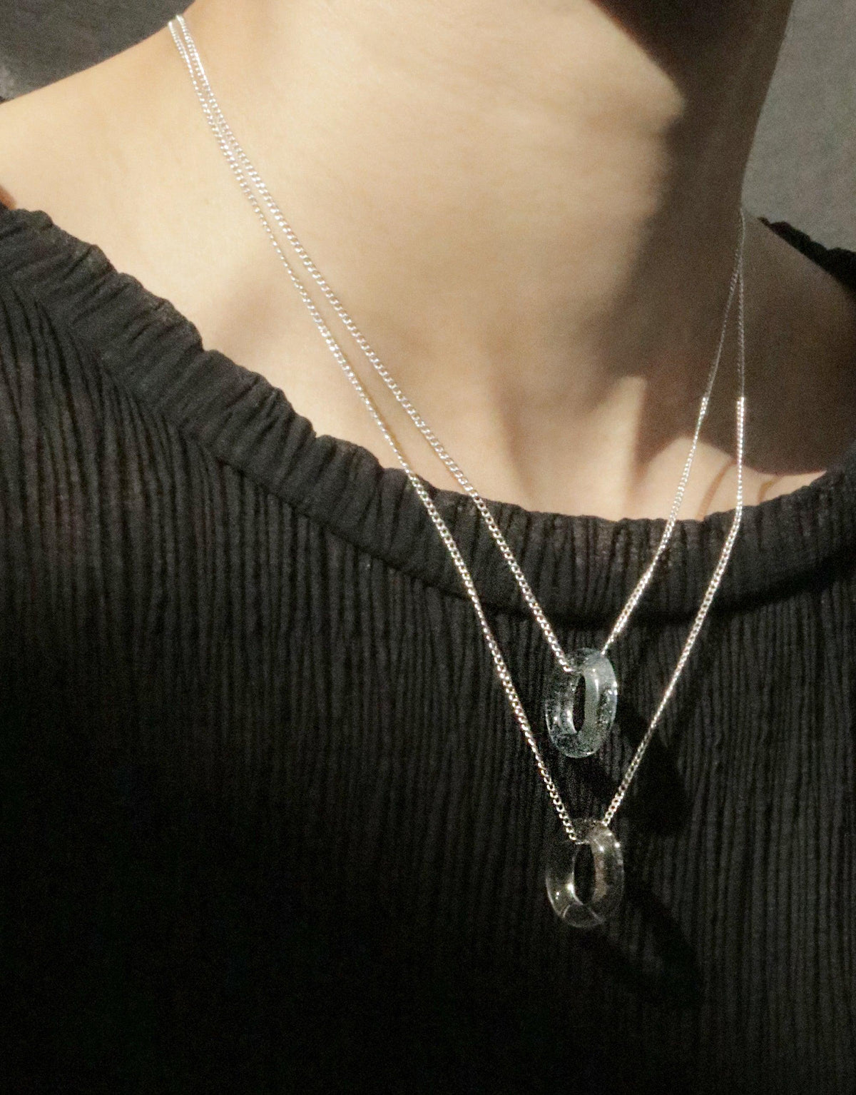 Elegant In The Loop Necklace featuring two delicate silver chains with transparent glass pendants, showcasing minimalist design against a black textured top. Eco-friendly and versatile accessory for everyday wear. CLED