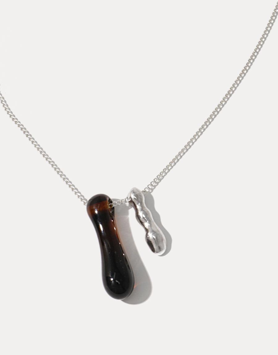 Sterling silver necklace featuring a handcrafted dark glass pendant shaped like a water drop, paired with a wavy metal charm. Elegant eco-friendly jewelry showcasing repurposed materials. Drop Counts Necklace by CLED