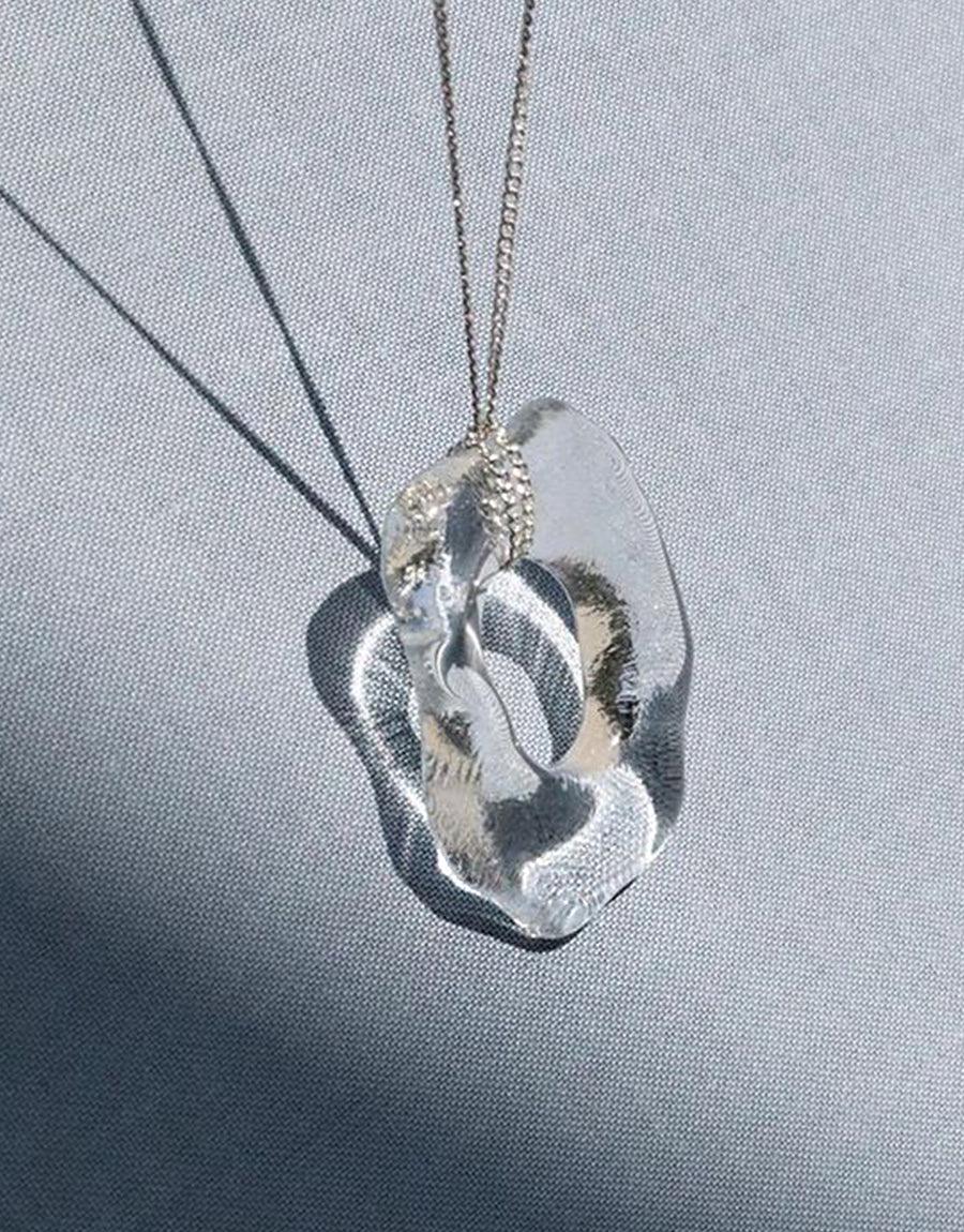 High Tide Necklace featuring a unique, organically shaped pendant made from repurposed glass. Sterling silver chain with a clear, wave-like Eco Gem pendant catching light. Handcrafted, sustainable jewelry piece showcasing ocean-inspired design. CLED