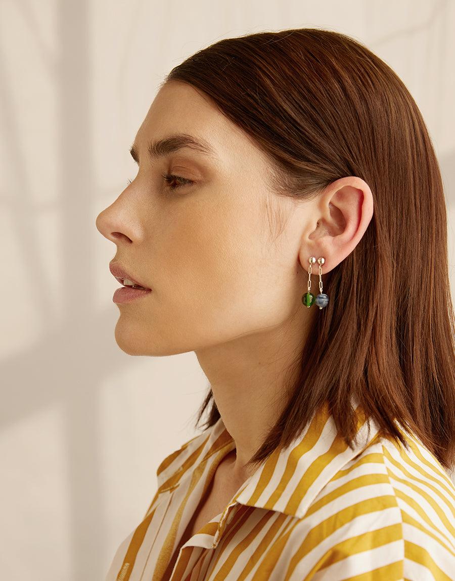 Elegant profile view showcasing Small Drop Earrings, featuring delicate sterling silver hooks with repurposed glass beads in green. Model wears striped yellow and white shirt, emphasizing the earrings' minimal and lightweight design. Handcrafted by CLED.