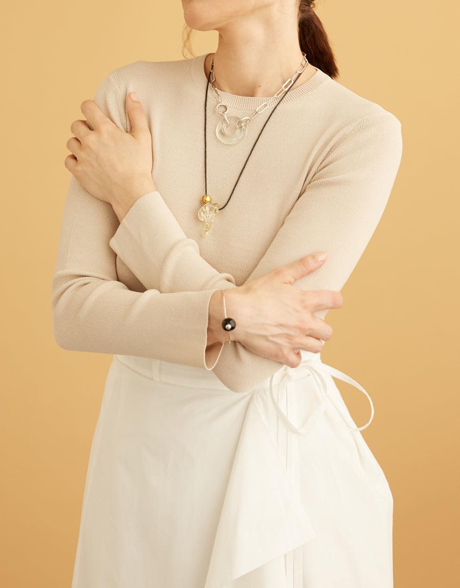 Elegant model wearing cream-colored dress showcasing Opening Necklace, featuring a unique torus-shaped pendant made from repurposed glass on a sterling silver chain. Complemented by a matching bracelet, embodying sustainable luxury. CLED Opening Necklace.