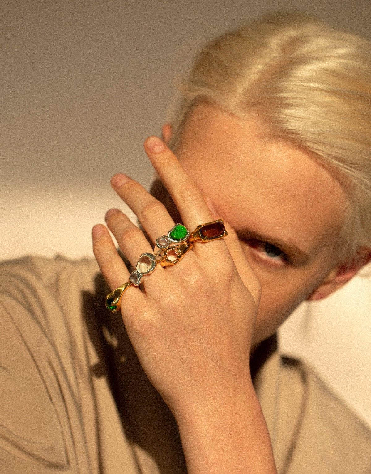 Close-up of a hand wearing multiple colorful rings, including the Prism Ring in Sterling Silver. The rings feature vibrant eco gems in various hues, showcasing the prismatic effect. Sustainable jewelry design by CLED.