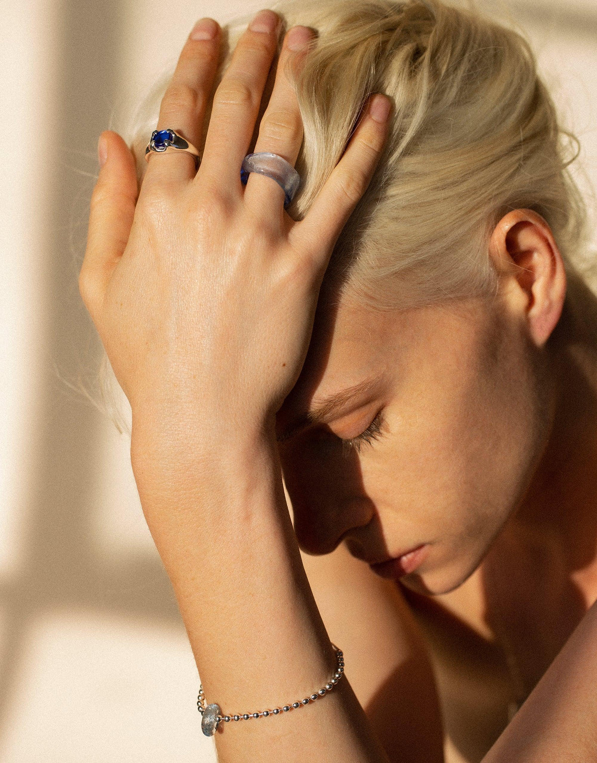 Close-up of a hand wearing the Beam Ring, showcasing its vibrant eco gem against soft, warm lighting. The ring complements other jewelry pieces, highlighting its versatility and elegance. Beam Ring by CLED.