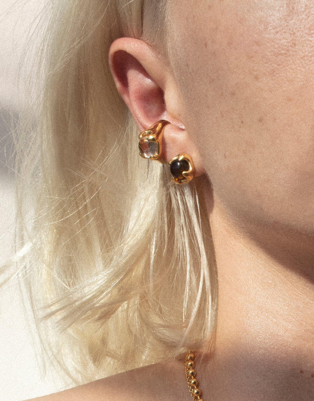 Close-up of gold Beam Earrings on a model with blonde hair, showcasing the unique design of eco-friendly jewelry made from upcycled glass. The earrings feature a sleek, modern shape that catches the light, embodying CLED's sustainable and stylish approach to accessories.
