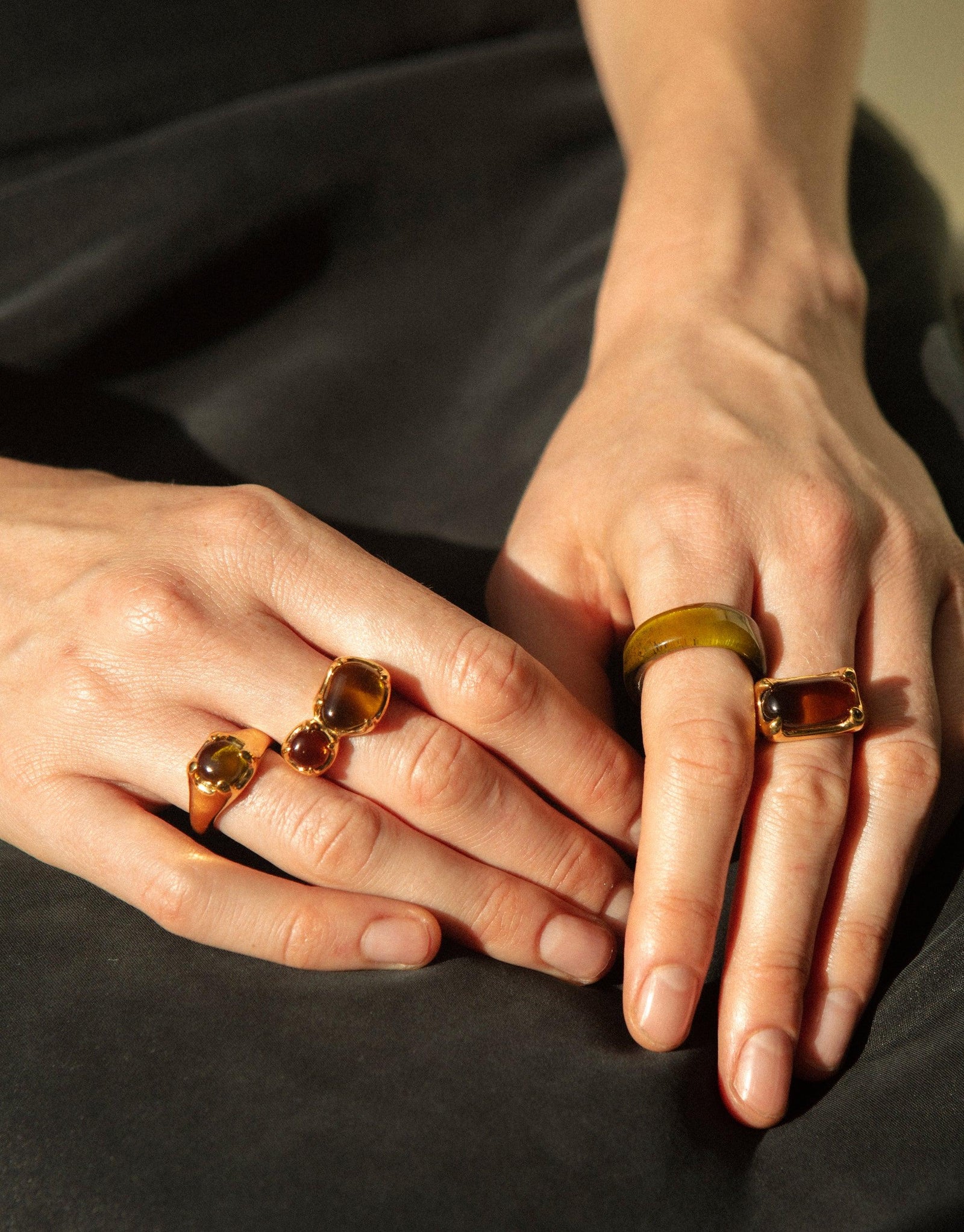 Hands wearing gold-toned rings with colorful eco gems, showcasing the Beam Ring collection. Unique handcrafted jewelry featuring upcycled glass gems in various hues, reflecting prismatic light effects. Sustainable and stylish accessories by CLED.