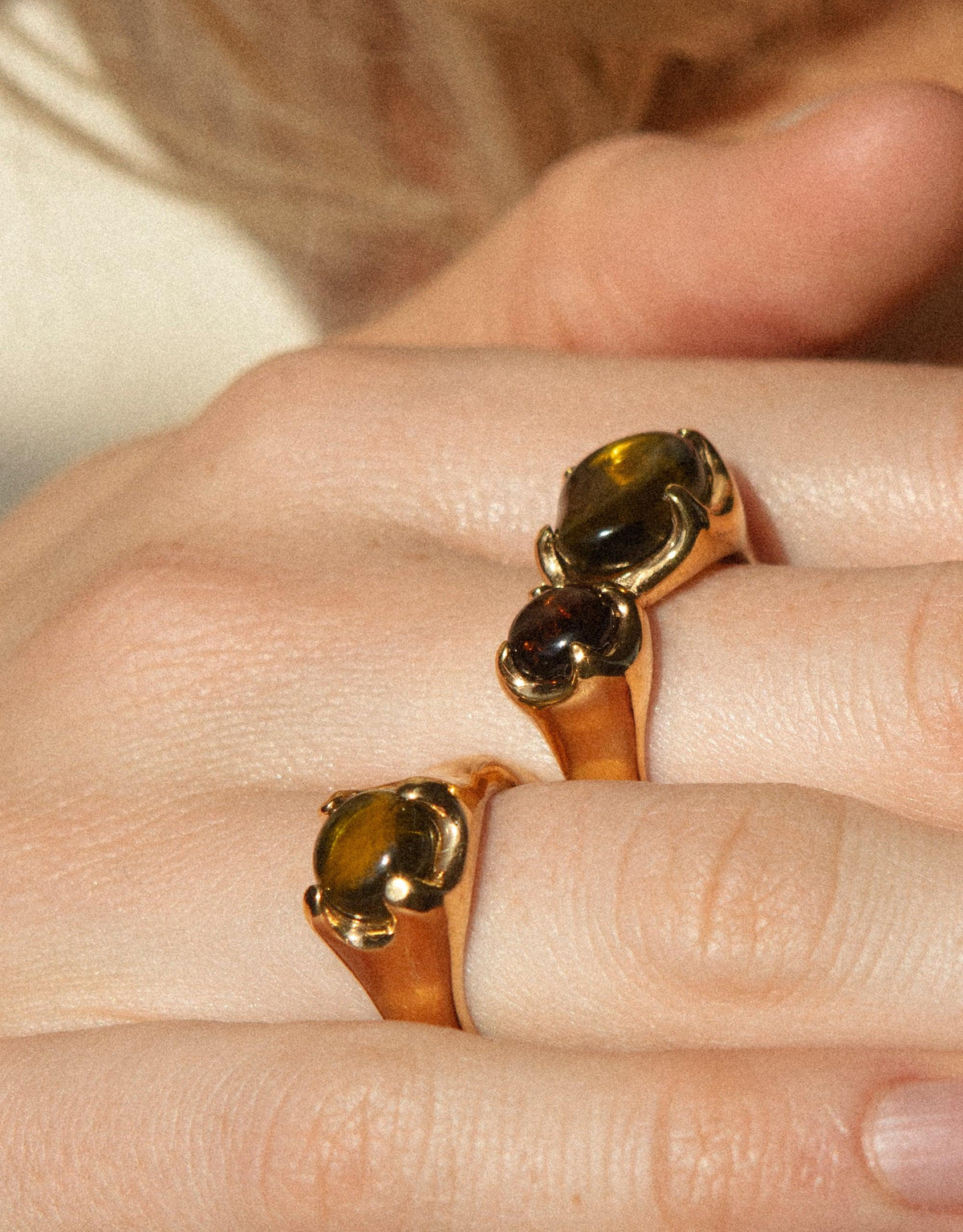 Close-up of hands wearing gold-toned Beam Rings featuring iridescent eco gems in various shades, showcasing the unique prism-like effect of the CLED sustainable jewelry collection. Beam Ring by CLED