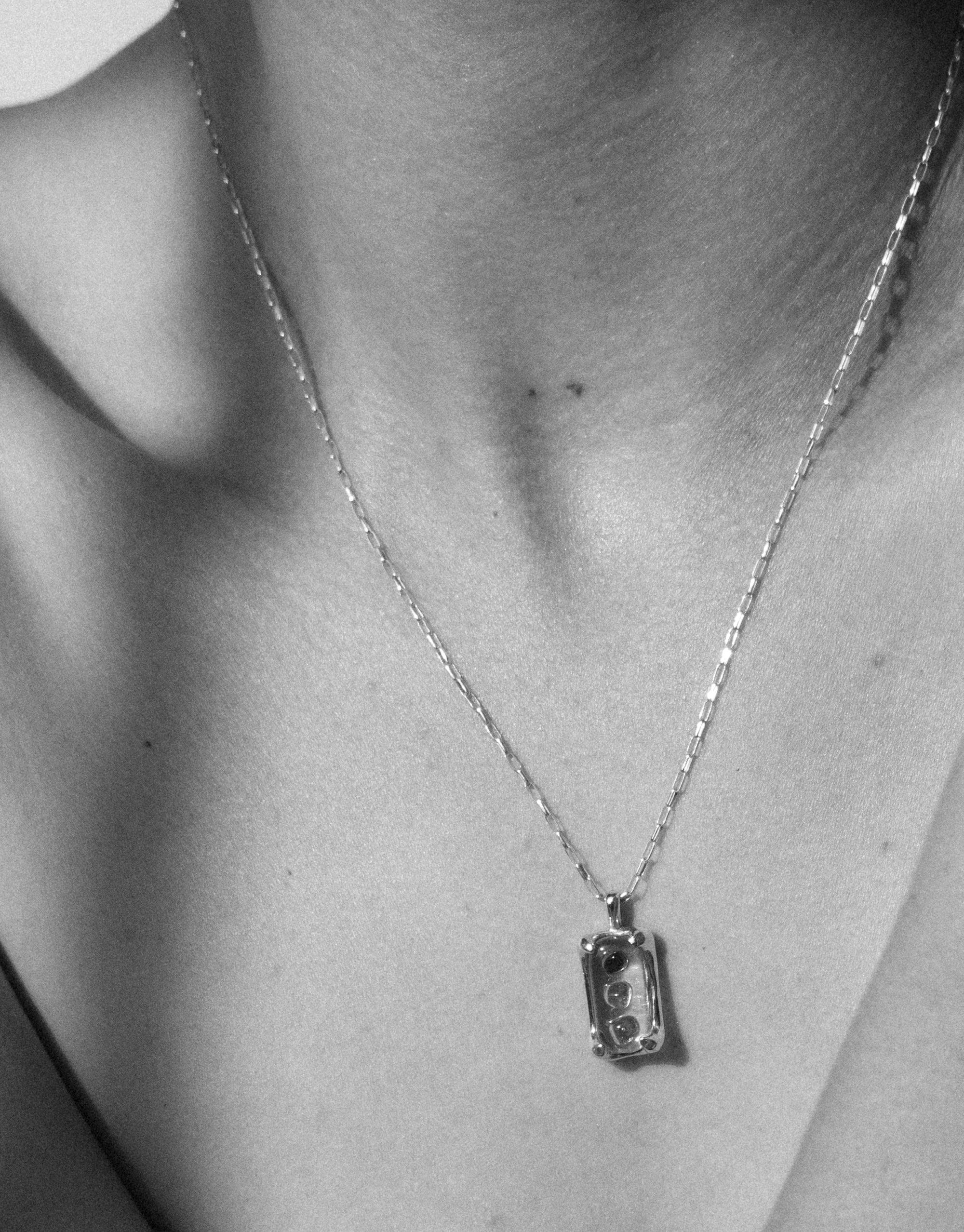 Close-up black and white image of a delicate chain necklace with a rectangular pendant, showcasing the elegant design of the Prism Necklace. The pendant features a unique eco gem detail, highlighting the sustainable craftsmanship by CLED.
