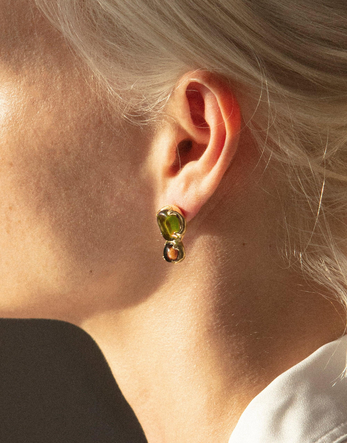 Close-up of Duo Beam Earrings featuring a vibrant green eco gem set in gold-plated brass, showcasing the unique prism-like design. The earring captures light beautifully, reflecting the sustainable and stylish ethos of CLED's handcrafted jewelry. Duo Beam Earrings by CLED.