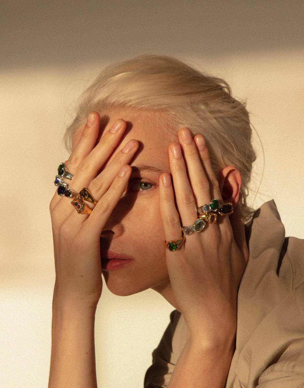 Gold plated Prism Ring showcased on model's hands covering face, displaying vibrant eco gems in various colors. Elegant design captures light, reflecting prismatic hues. Sustainable jewelry piece handcrafted from upcycled glass. Prism Ring | Gold Plated by CLED.