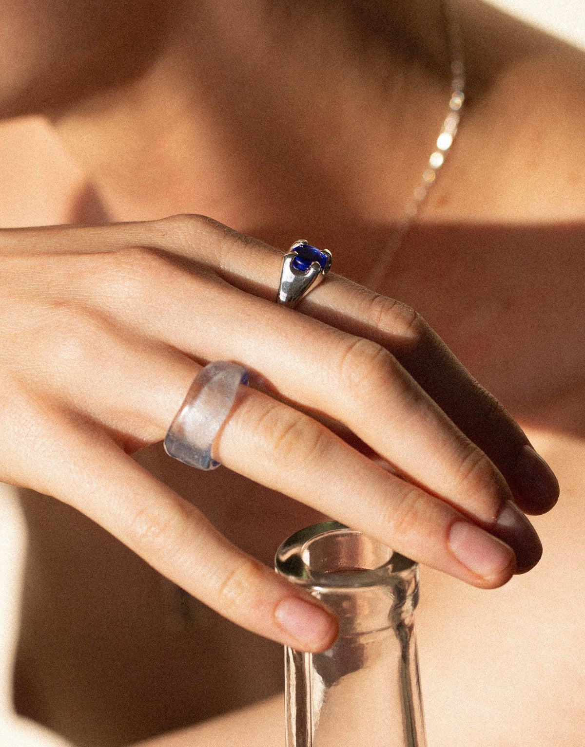 Close-up of hands wearing silver rings, including the Beam Ring with a blue eco gem, showcasing sustainable jewelry design. Sunlight casts a warm glow, highlighting the unique craftsmanship of handmade rings by CLED.