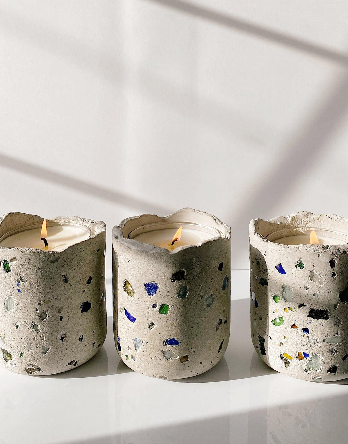 Handcrafted concrete vessels with colorful glass fragments, containing lit soy wax candles. Sustainable and stylish LAIT X SHIPPE X CLED Vessel & Candle collaboration, showcasing upcycled materials and artisanal craftsmanship. CLED